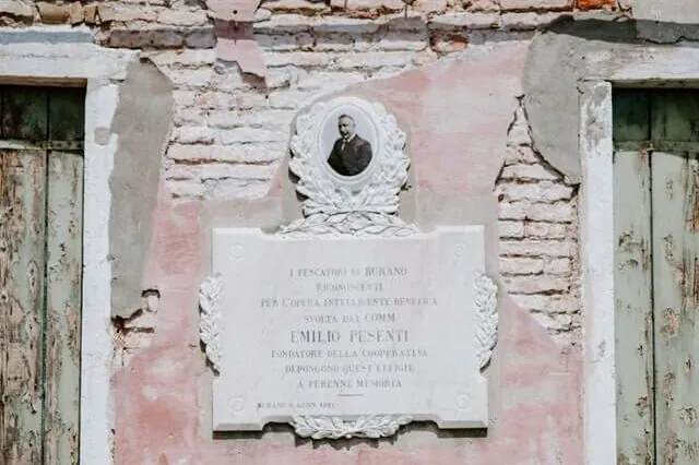Weathered pink stucco wall with marble plaque bearing Emilio Pesenti portrait and Italian inscription