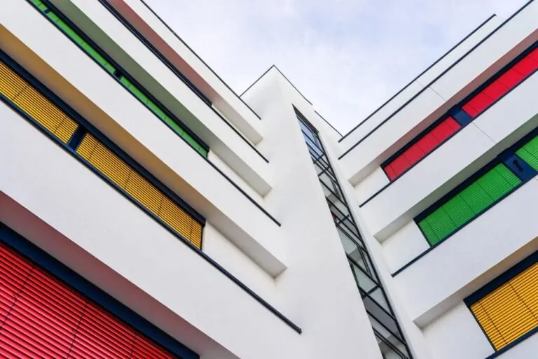 Contemporary white multi‑story stucco facade with bold red, yellow, and green window shutters adding dynamic contrast