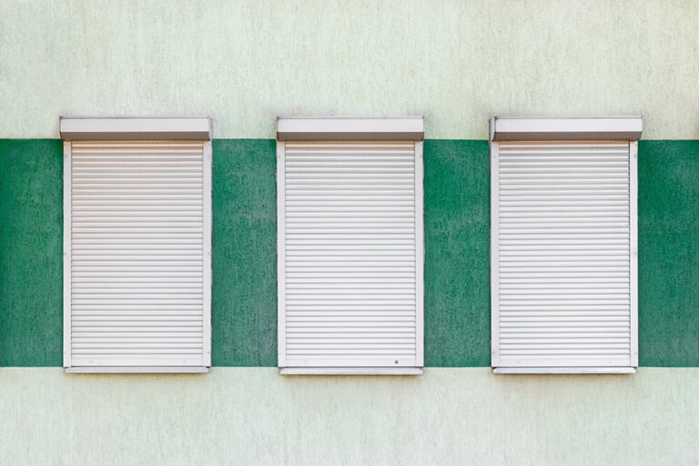 Three closed white roller shutters set within a horizontal green stucco stripe on a light-colored wall