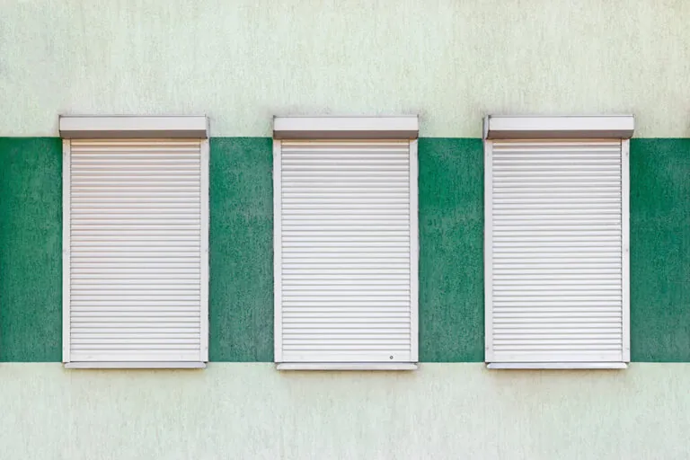 Three closed white roller shutters set within a horizontal green stucco stripe on a light-colored wall