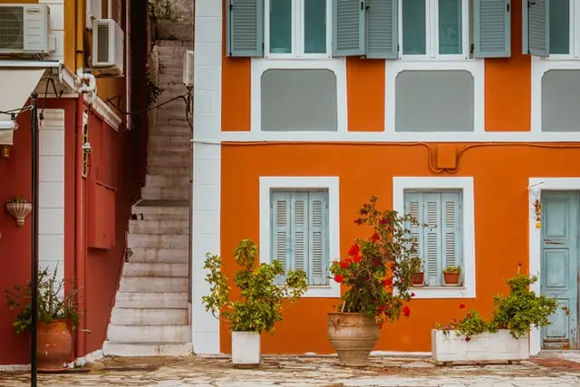 Orange and brown stucco facade with shuttered windows, white trim, potted plants and narrow exterior stairs