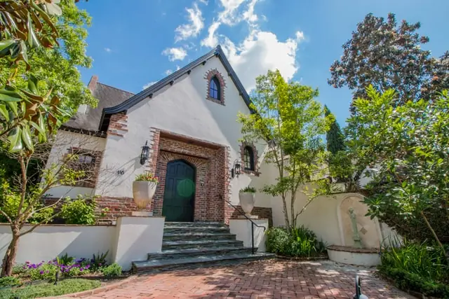 White stucco home with steep pitched roof, brick arched doorway, brick steps, arched window and greenery
