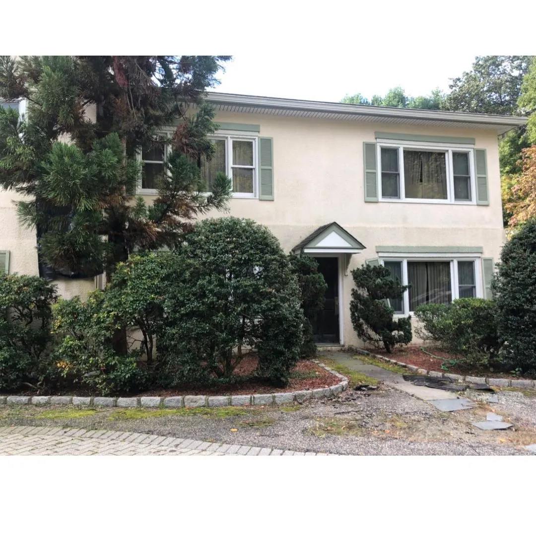 Boonton NJ 7 Two-story home in Boonton NJ with aged stucco exterior, faded shutters, overgrown landscaping, and walkway damage