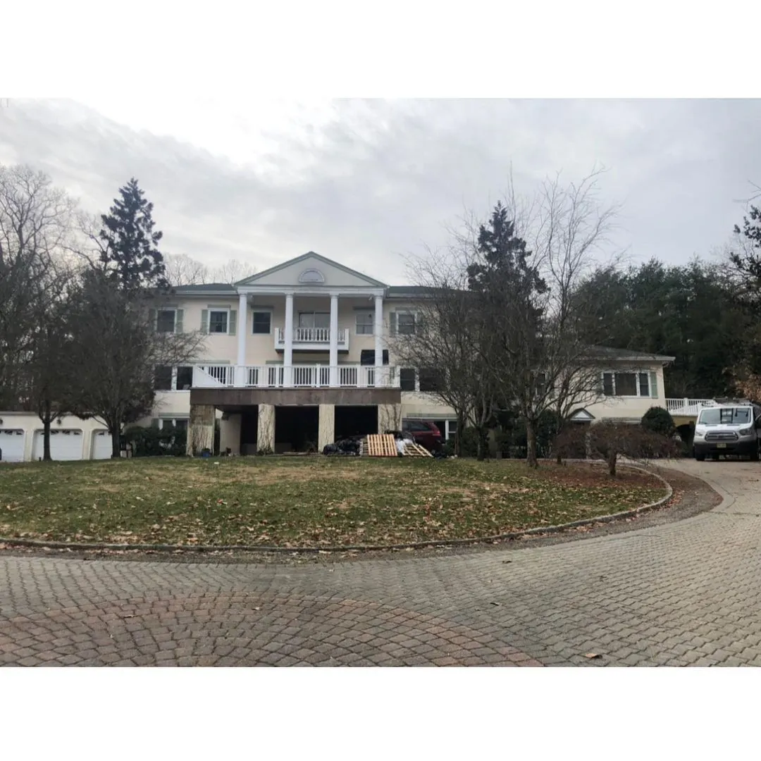 Boonton NJ 5 Spacious colonial-style stucco house with columns, garage openings, bare trees, and renovation materials visible