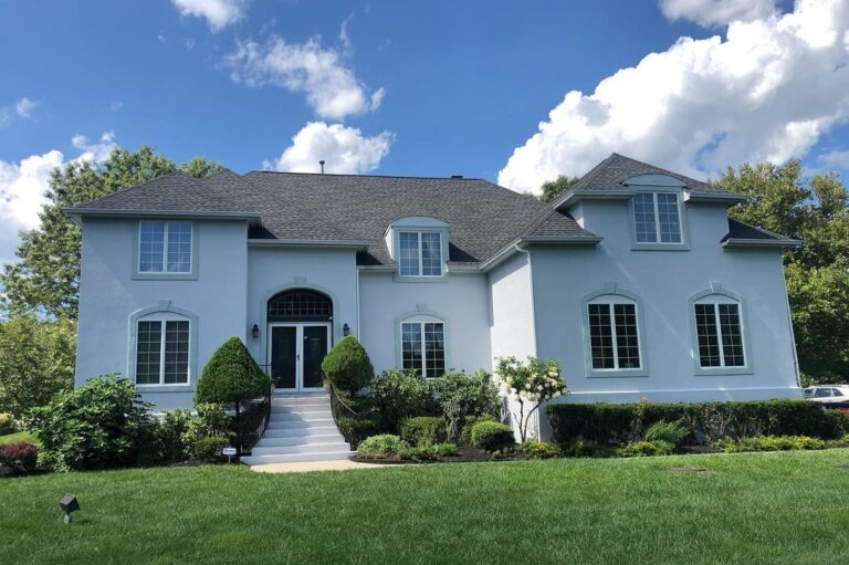 Front view of a two-story stucco house with gray finish, arched windows, manicured lawn, and blue sky backdrop