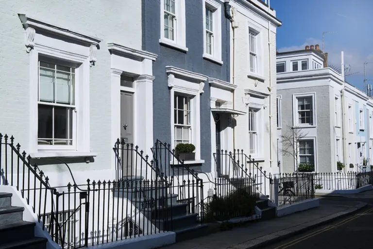 Row of classic stucco-clad townhouses with ornate trim, iron railings, and pastel-colored facades in city block