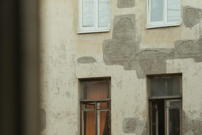 Old building facade with mismatched stucco patches, exposed brick, and paint damage showing improper repairs