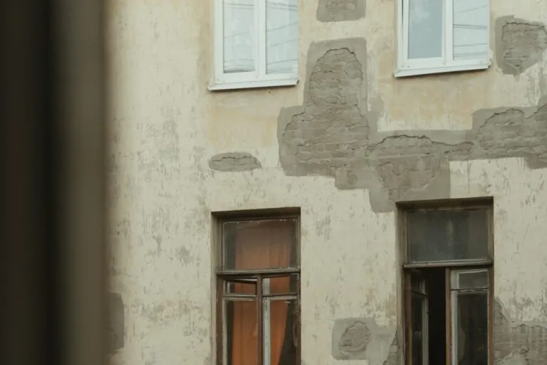 Old building facade with mismatched stucco patches, exposed brick, and paint damage showing improper repairs