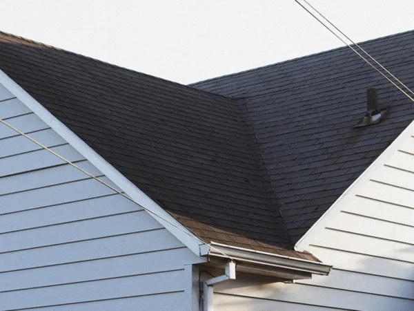 Asphalt Roof and Gutter on Home with Light Siding Shingled roof and functional gutter system installed on house with light blue siding and blooming flowers