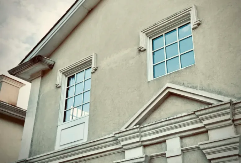 Close-up of exterior wall with visible stucco cracks, patchwork lines, and mismatched window trim detailing