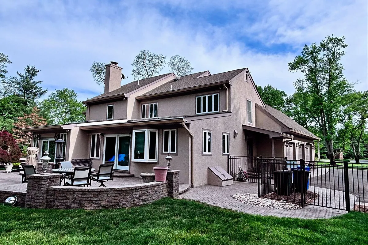 Backyard facade of Moorestown home with freshly restored stucco, windows, and surrounding landscaping