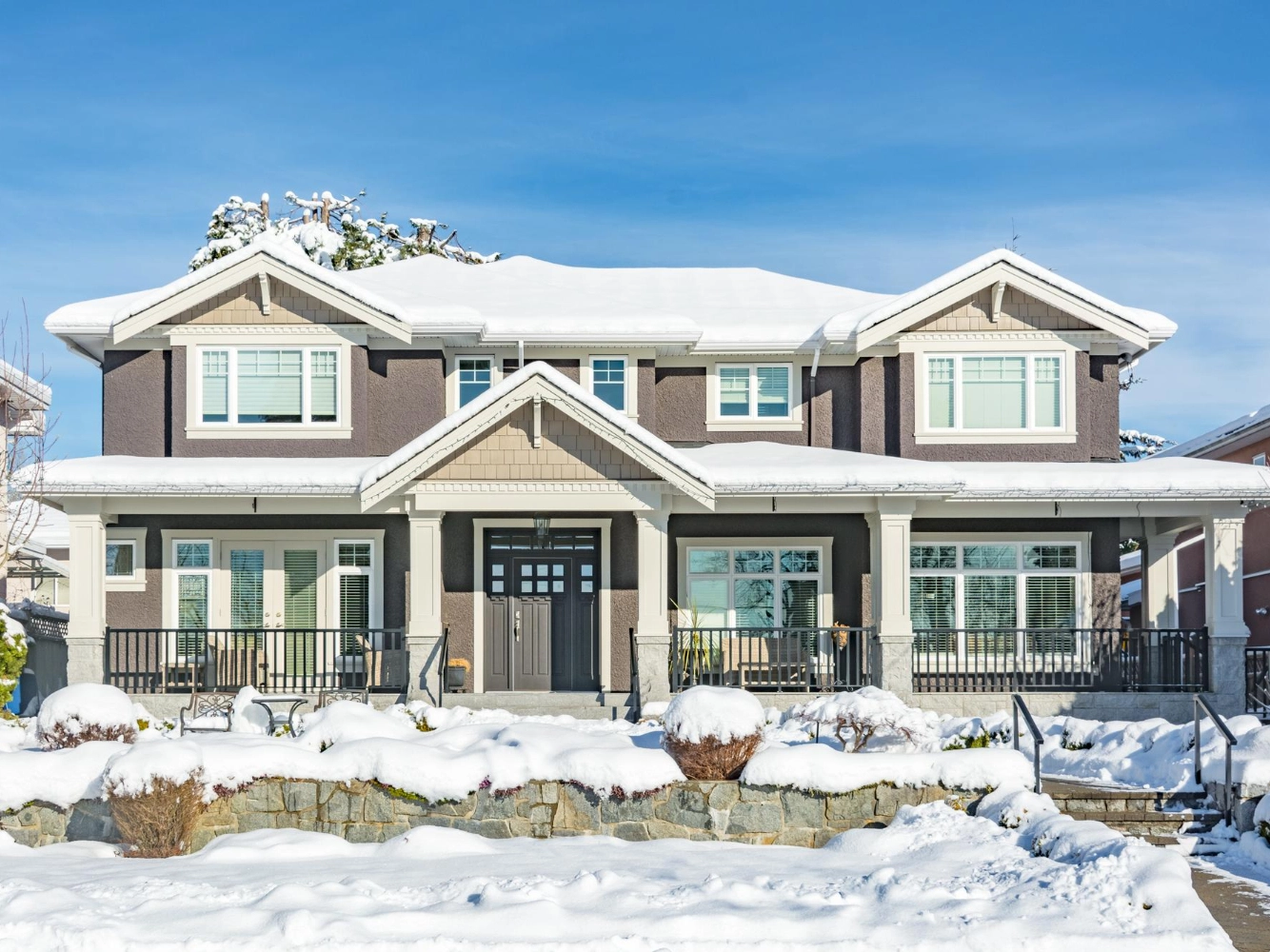 Large two-story home with dark stucco walls, columns, and a snow-covered roof and landscaping