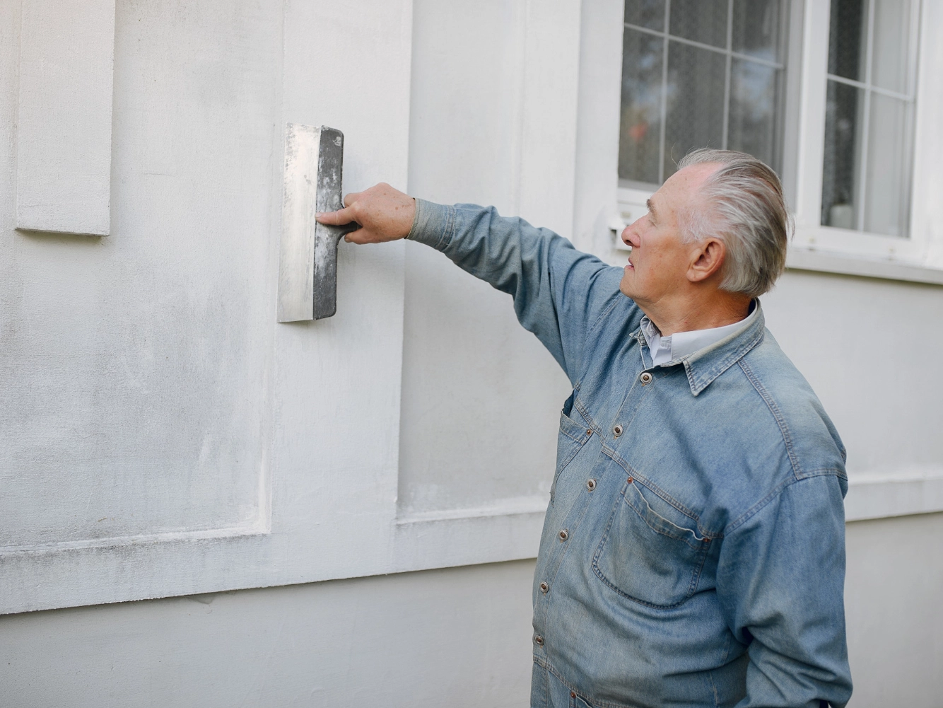 How to Prevent and Remove Mold on Stucco 4 Technician smoothing a stucco finish with a trowel near a window on a light-colored facade