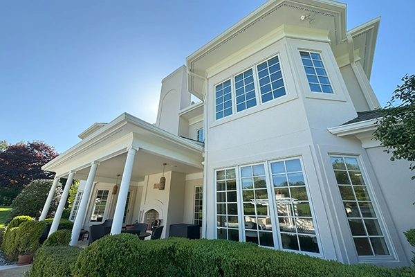 ZD Stucco Repair — Residential Stucco Refresh, Mendham, NJ Rear elevation with light stucco walls, tall windows, and a covered patio with columns; project by ZD Stucco Repair in Mendham, NJ.