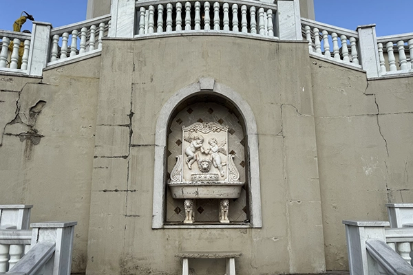 Stucco crack repair on architectural wall Large exterior stucco wall with visible cracks and a recessed decorative niche before restoration