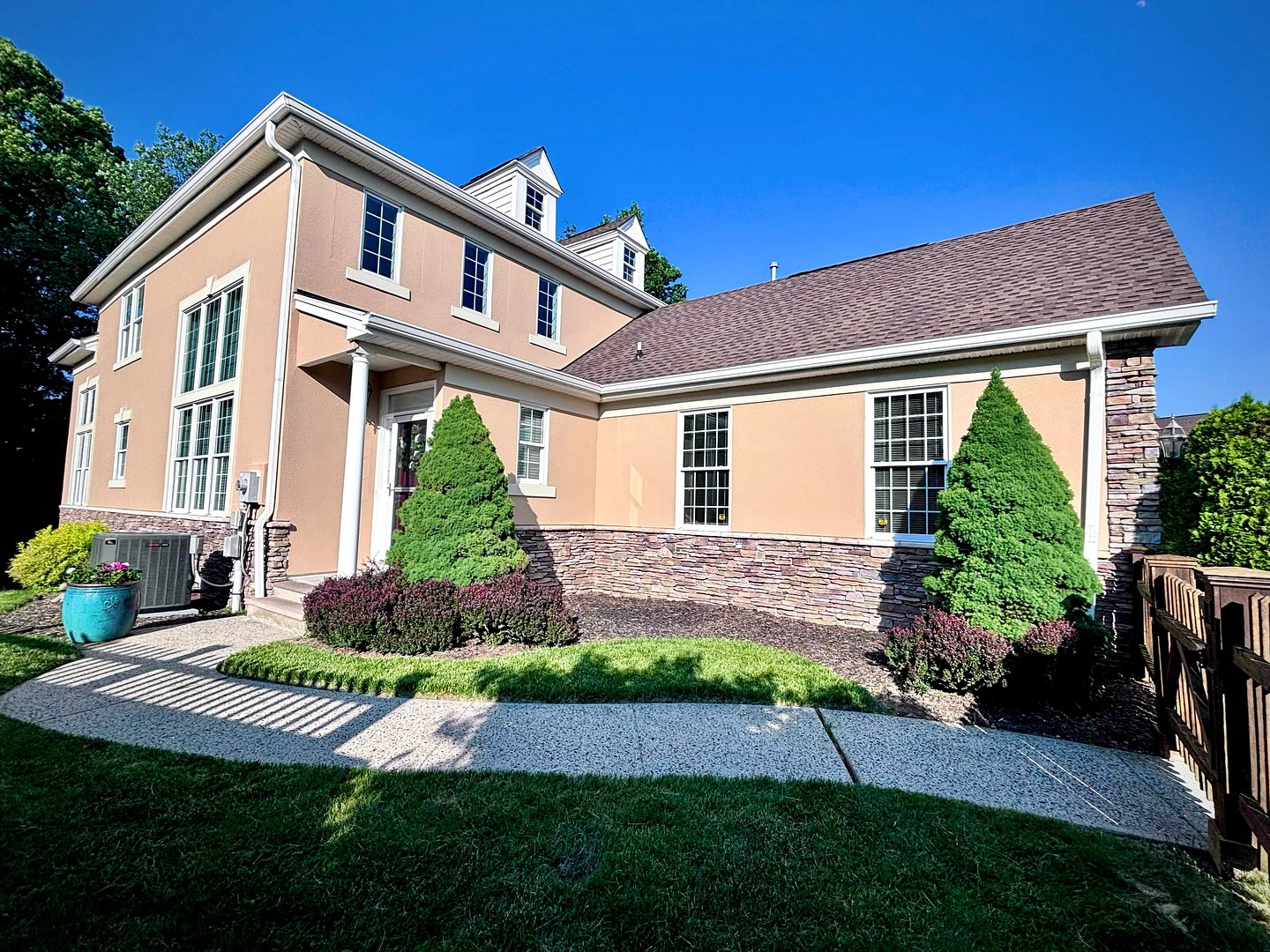 Light tan stucco exterior with a stone base, white trim, and a sunny front yard walkway.