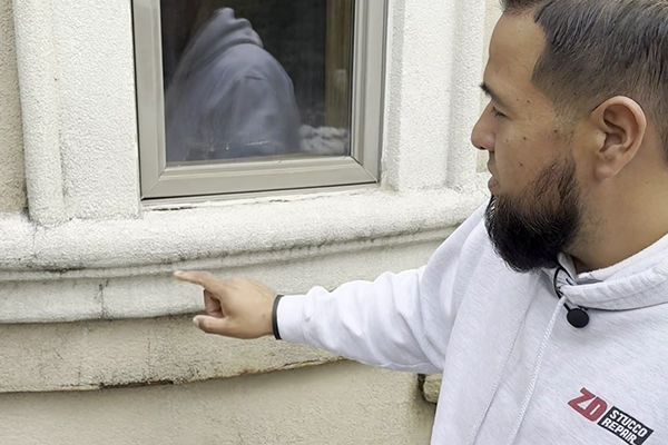 ZD Stucco Repair — stucco inspection at window sill Specialist from ZD Stucco Repair pointing out wear and staining on stucco around a window during an exterior inspection