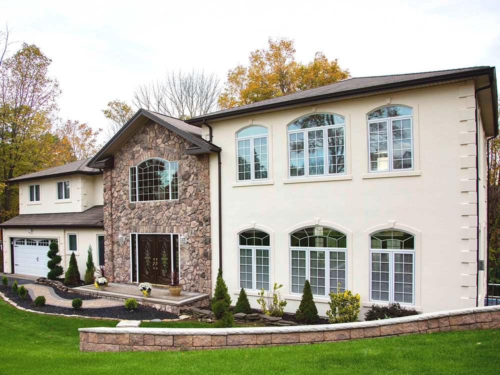 Large residence featuring light stucco, a full-height stone entry, and multiple arched windows.