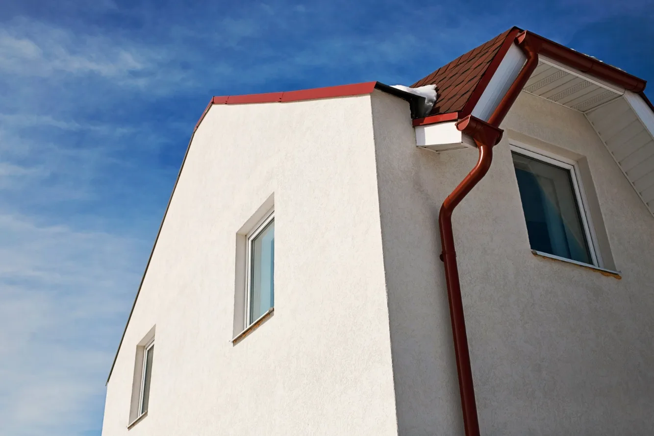 White stucco house with a gable roof and red gutters under blue sky, small snow on the eaves, New Jersey