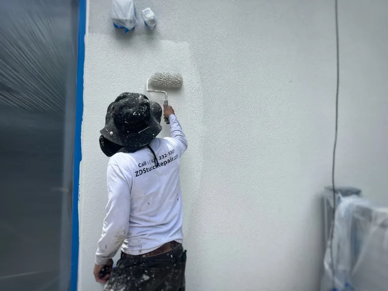 Worker rolling paint onto an exterior stucco wall