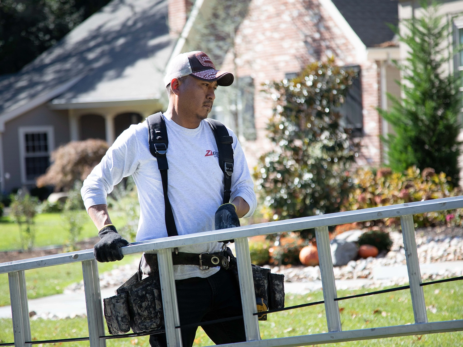 ZD Stucco Repair — field technician with ladder Technician carrying a ladder and tool belt at a residential job site.