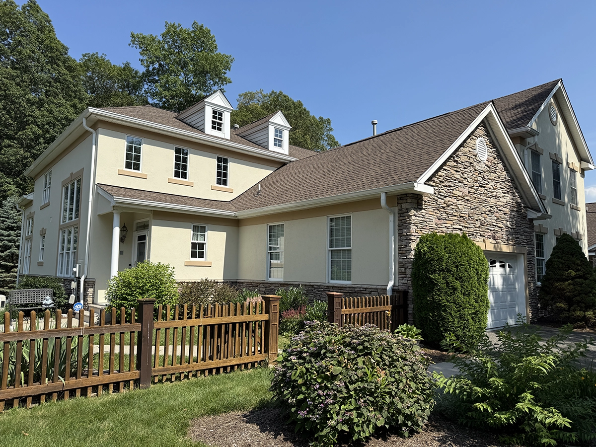 Two-story cream stucco home with a stone gable accent and dormers behind a picket fence; project by ZD Stucco Repair in Chester, NJ.
