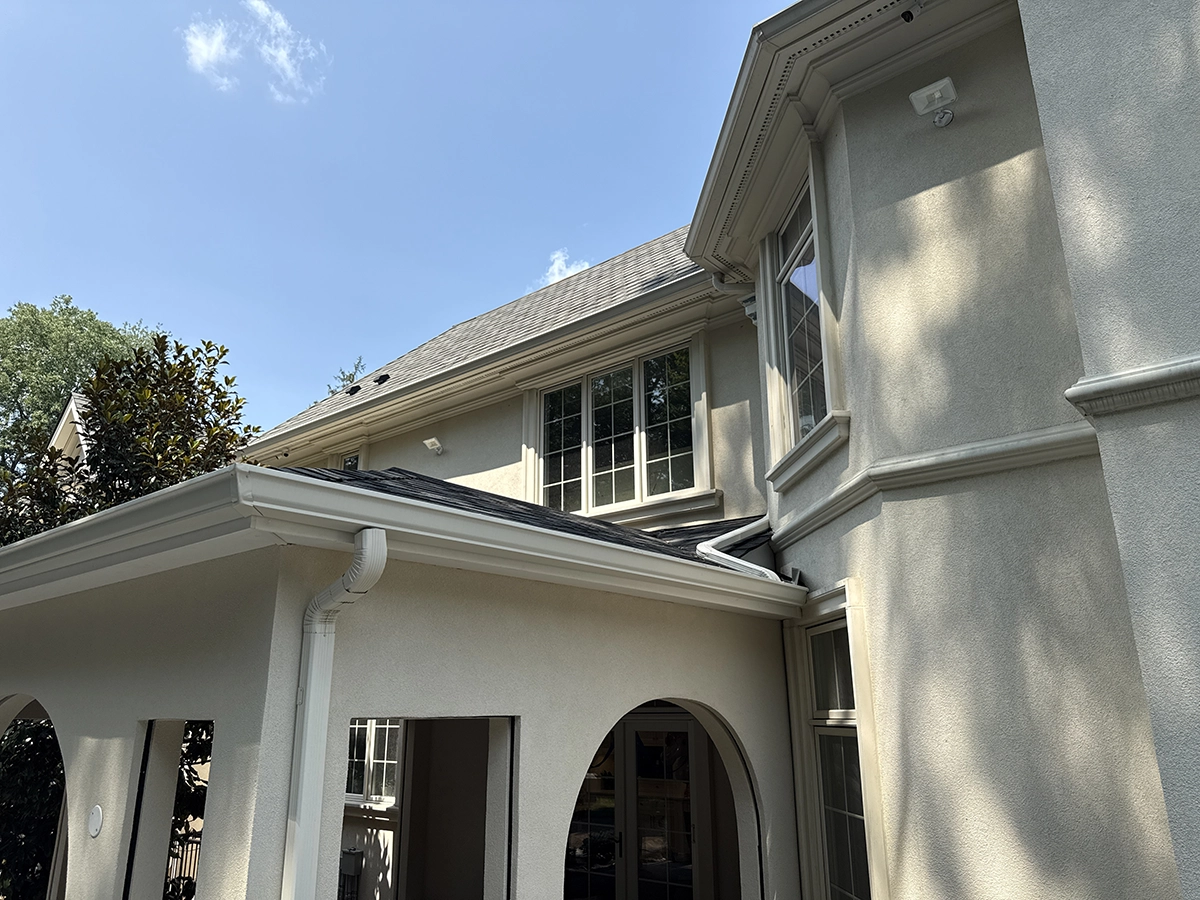 Stucco facade with arched patio and detailed eaves — Demarest, NJ Light-colored stucco walls with crisp trim, gutters, and arched openings under a clear sky in Demarest, NJ.