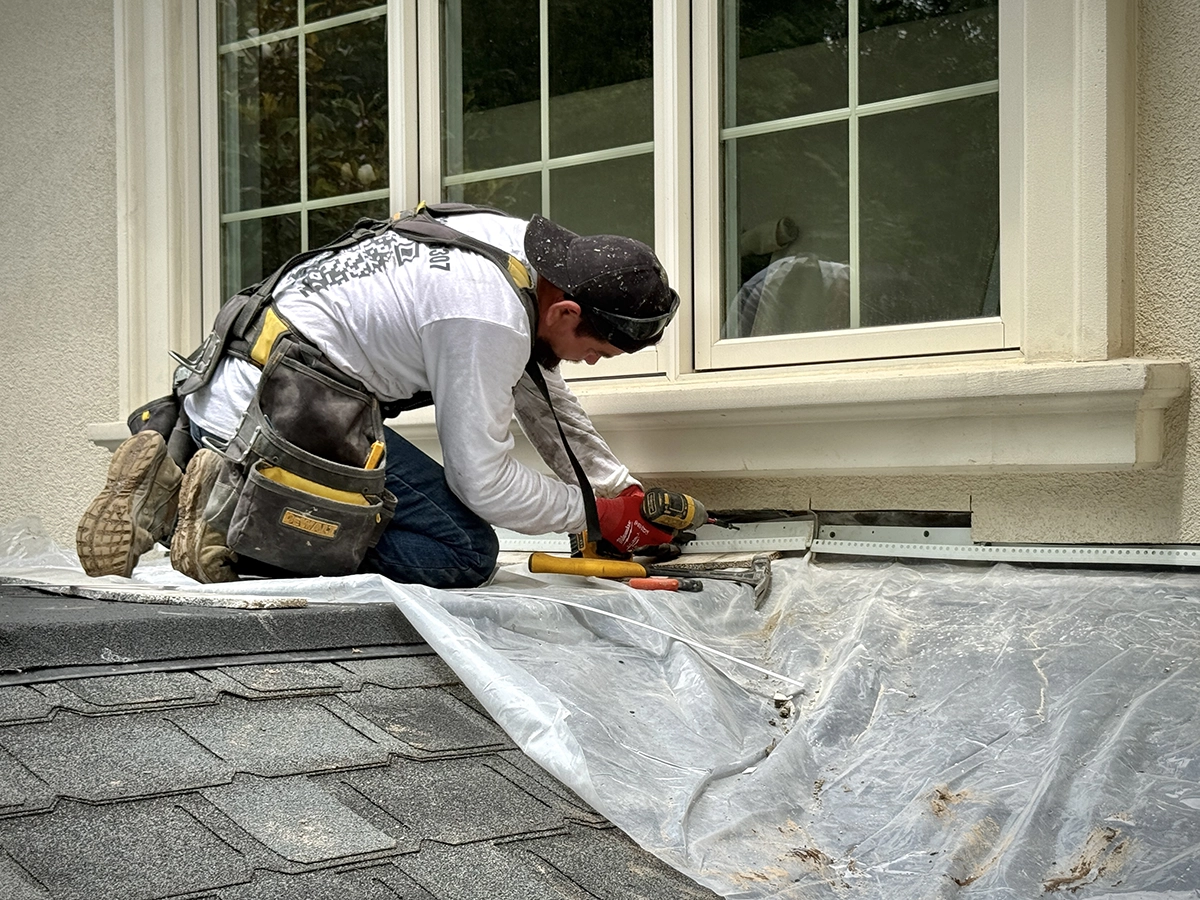Stucco window detail — flashing and weep screed installation, Demarest, NJ Worker fitting metal flashing and weep screed below a window on a stucco facade to improve water management in Demarest, NJ.