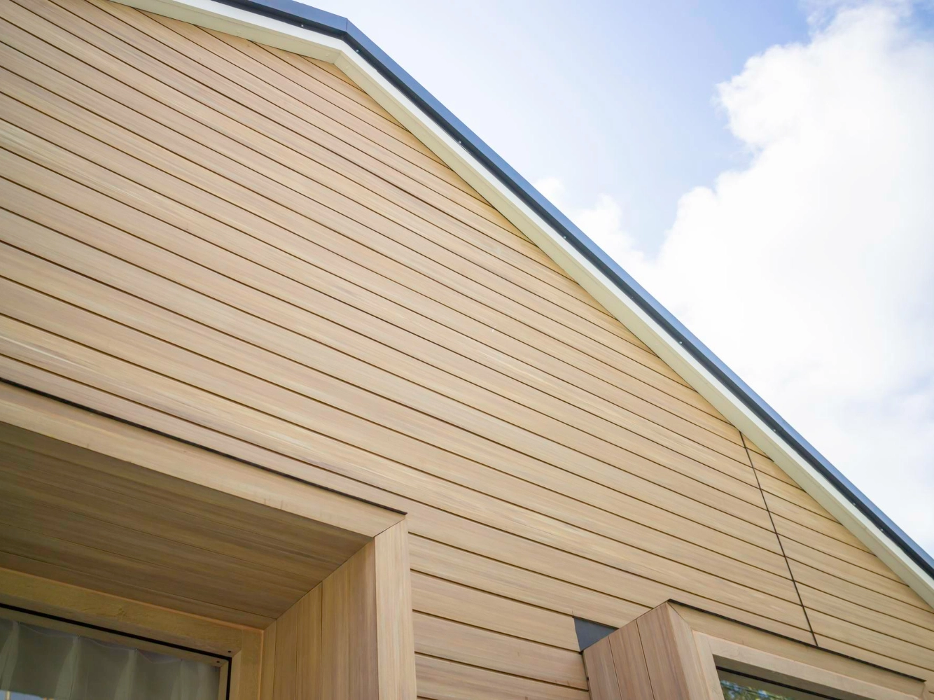 Close view of horizontal wood-look vinyl siding on a gable with metal coping under a blue sky
