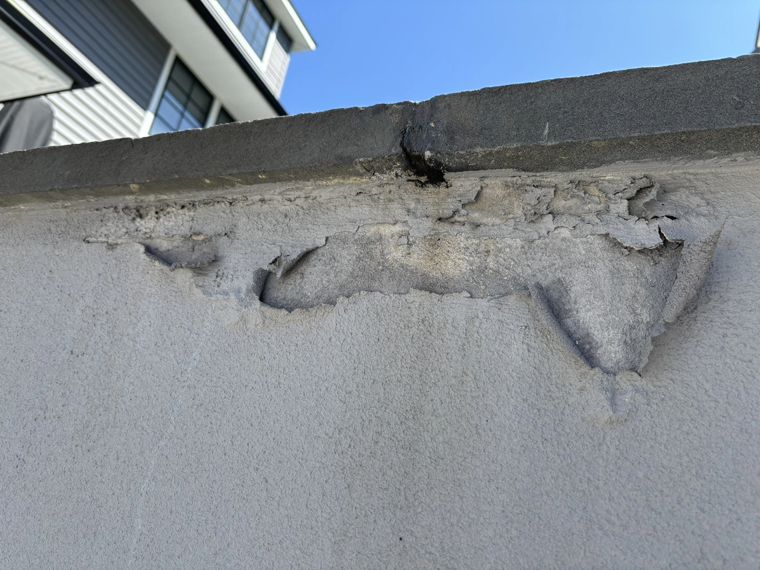 Close detail of a wall cap where stucco has cracked and peeled away, exposing base coat and substrate; typical moisture entry point.