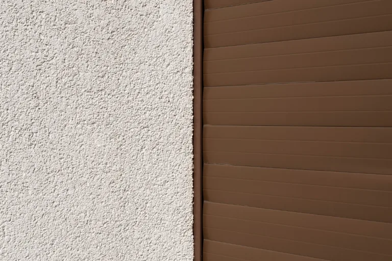 Closeup of a light stucco wall next to brown horizontal siding with a clean vertical joint