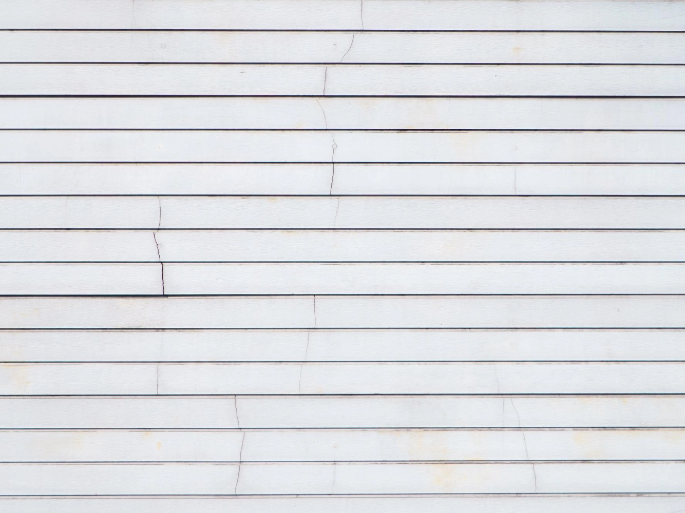 White horizontal lap siding showing fine cracks and slight staining across several boards