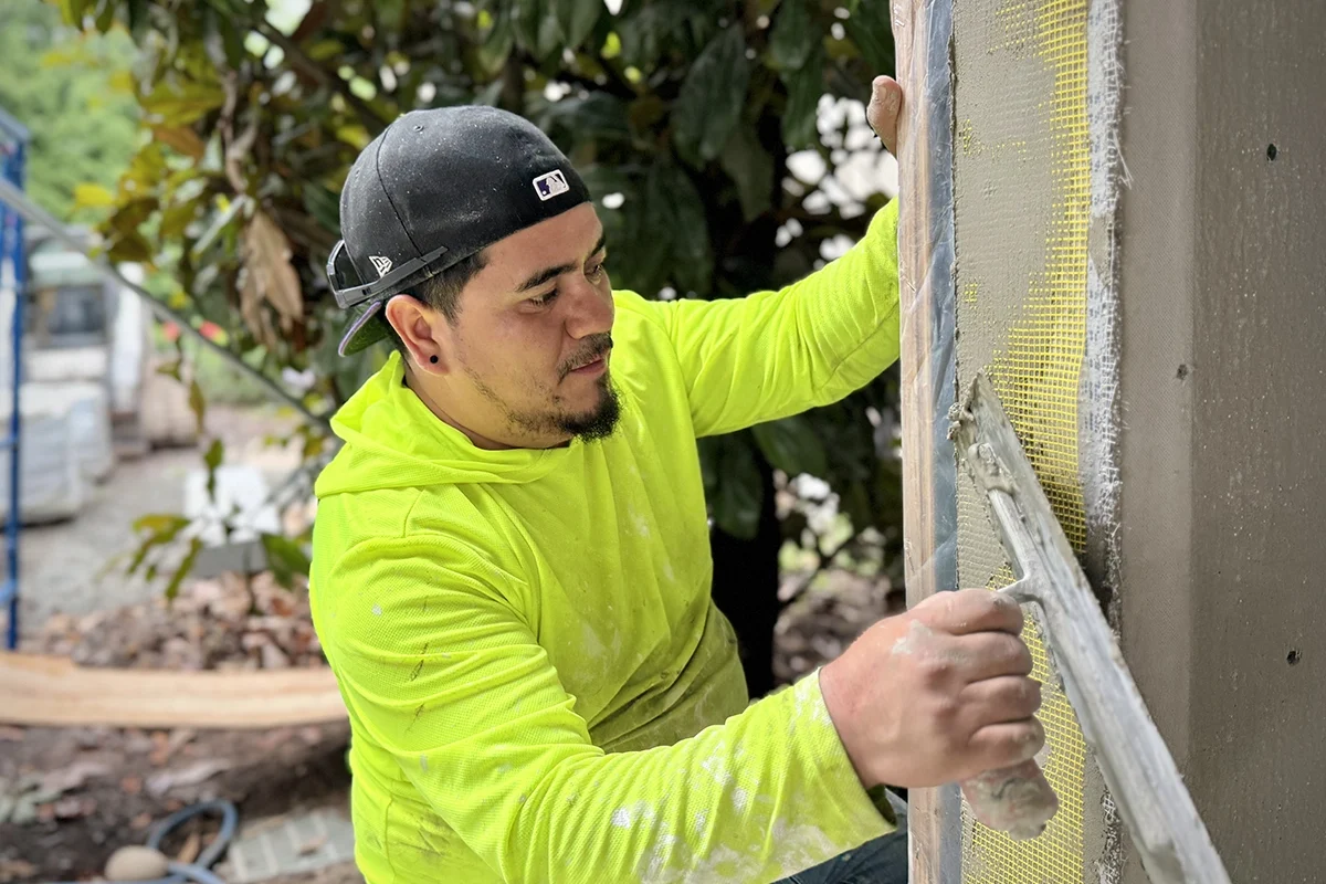 ZD Stucco Repair technician embedding fiberglass mesh into a stucco/EIFS base coat on an exterior wall, close-up.