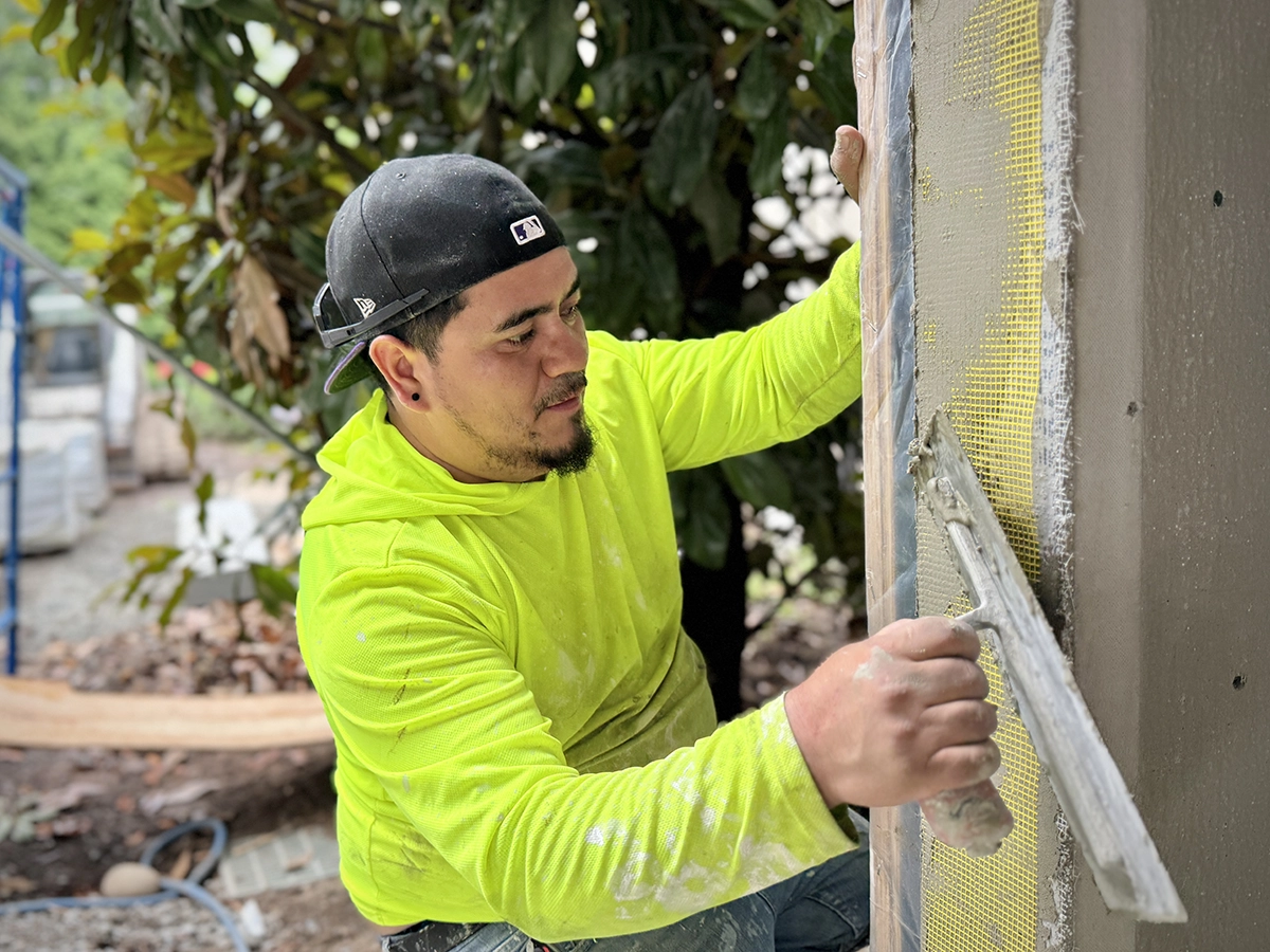 ZD Stucco Repair technician embedding fiberglass mesh into a stucco/EIFS base coat on an exterior wall, close-up.