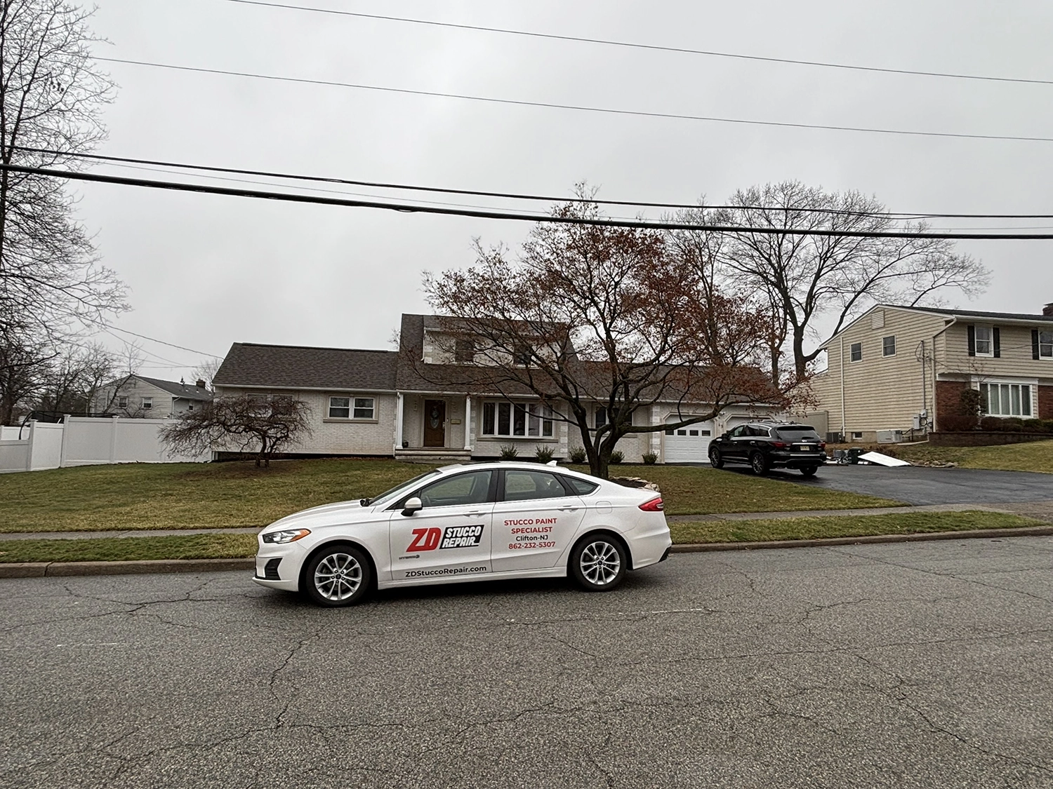 Company sedan with ZD Stucco Repair branding parked on a suburban street in front of a single-family home on an overcast day, ready for inspection and repair.