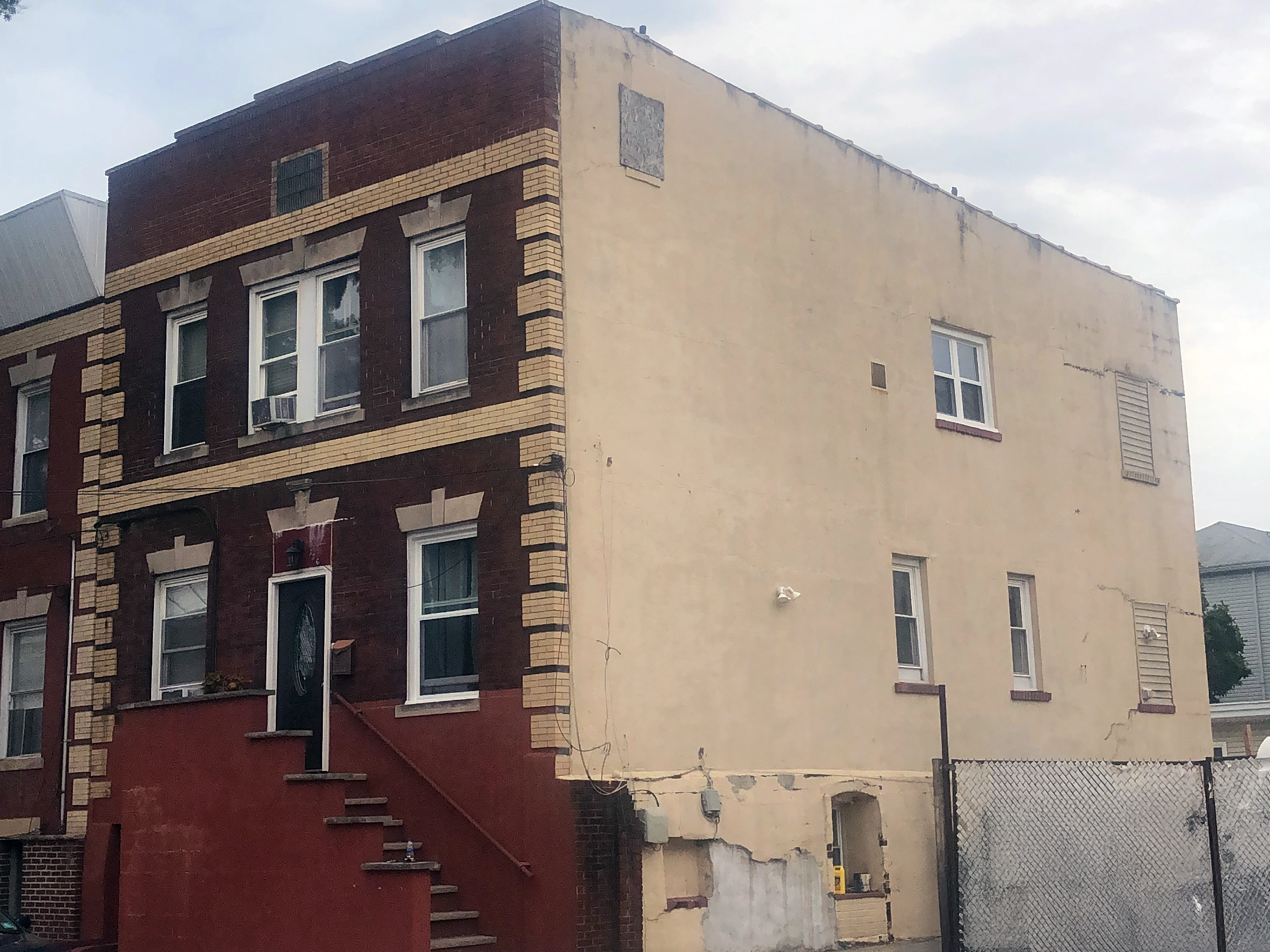 Does Stucco Add Value to Your Home? 5 Side of a Newark brick rowhouse with deteriorated stucco—cracks, patches, and peeling areas—prior to professional repair.