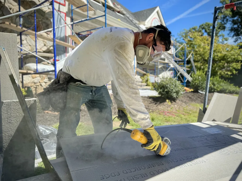 Technician from ZD Stucco Repair cutting cement board while wearing PPE during a commercial facade restoration.