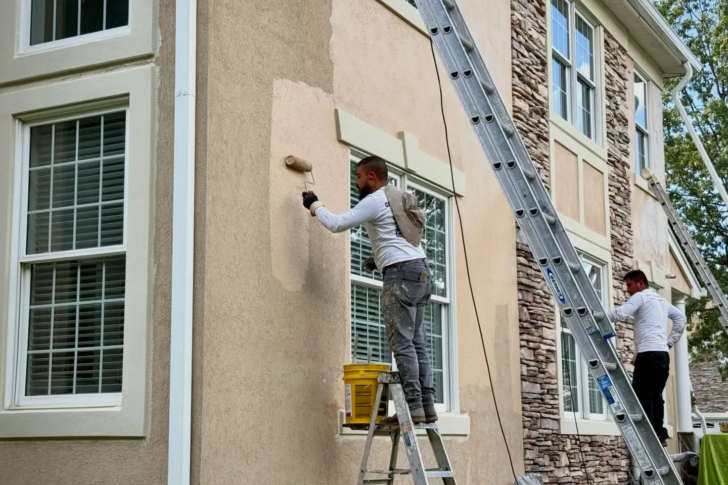 Professional painters on ladders rolling elastomeric paint onto a stucco wall