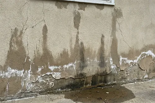 4 Complex Stucco Problems in New Jersey and How ZD Stucco Repair Fixes Them 7 Water-damaged stucco wall with cracks, dark moisture stains, and white efflorescence near the base