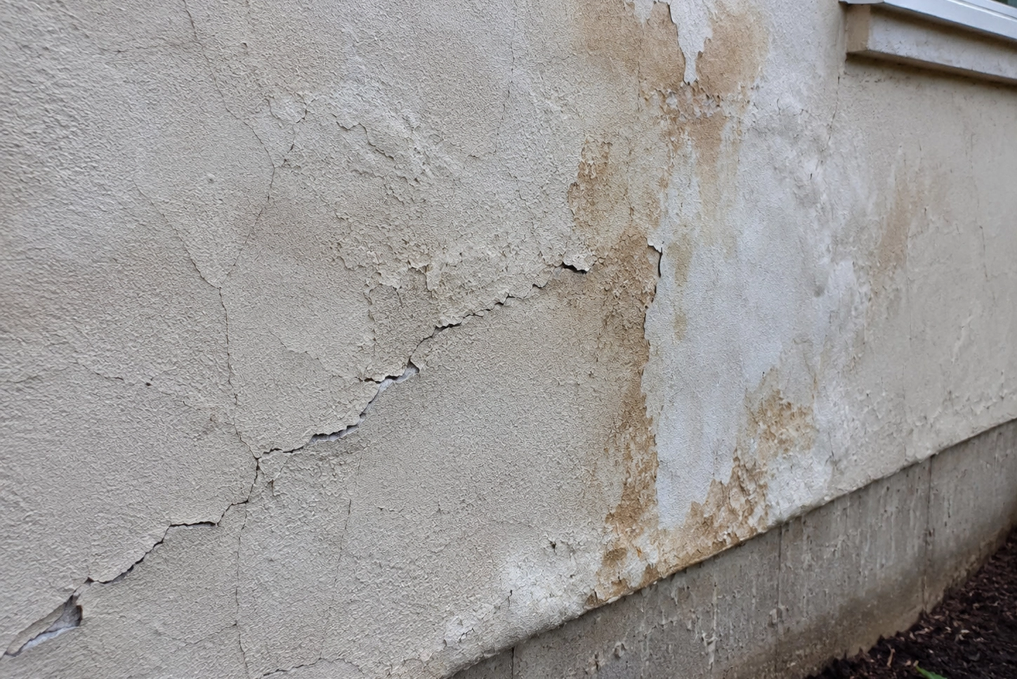 Cracked and stained exterior finish showing possible water intrusion