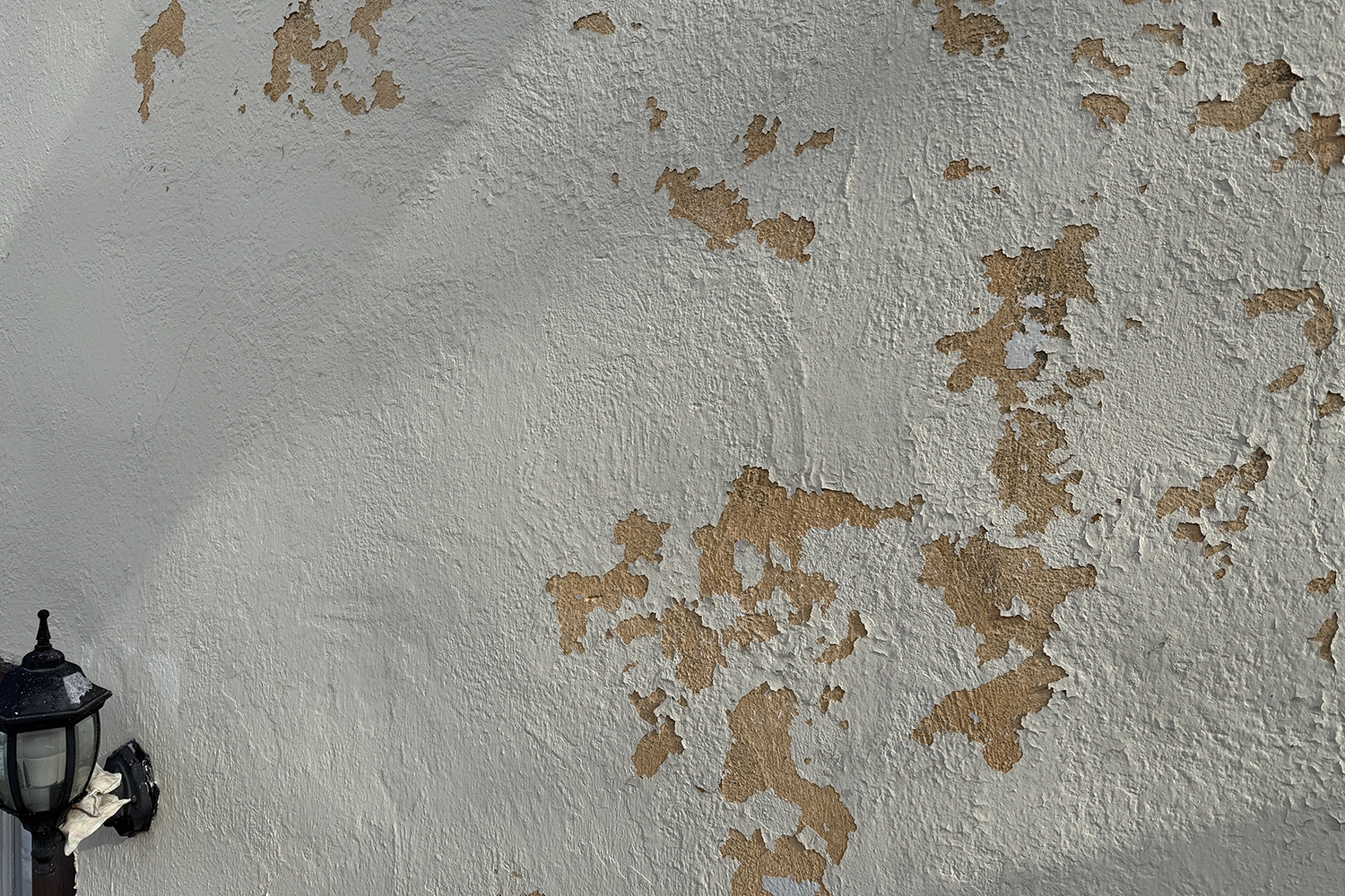 Extreme close-up macro photograph of peeling stucco paint showing texture, separation, and deterioration caused by moisture penetration and coating failure