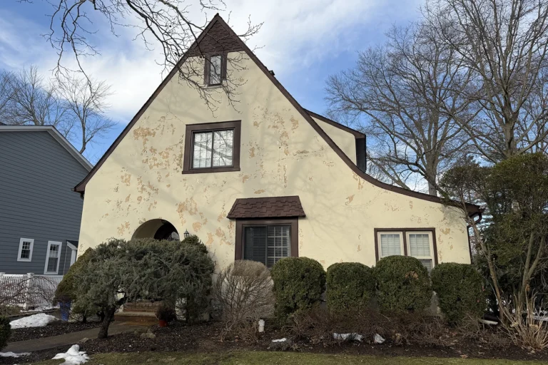 Detailed close-up view of peeling stucco paint showing extensive water damage, discoloration, and coating failure patterns on residential exterior wall