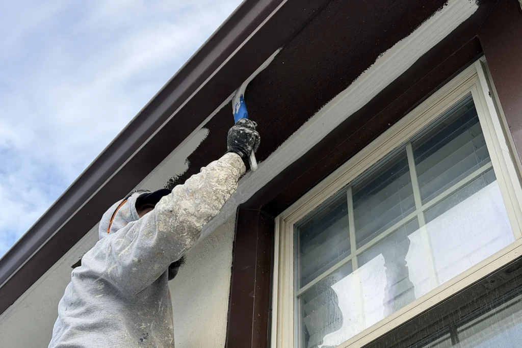 Is Your Home Exfoliating? What Peeling Stucco Really Means 4 Professional contractor wearing protective gear applying fresh protective coating to prepared stucco wall surface using professional painting technique