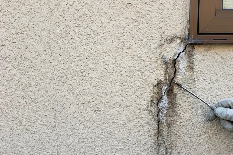Diagonal crack in stucco with brown rust stains indicating water infiltration and metal oxidation behind the surface