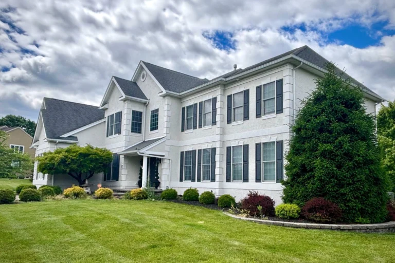 Fully restored two-story home in Flemington NJ with pristine white stucco facade, featuring multiple large windows, professional landscaping, and properly sealed exterior after complete stucco restoration project