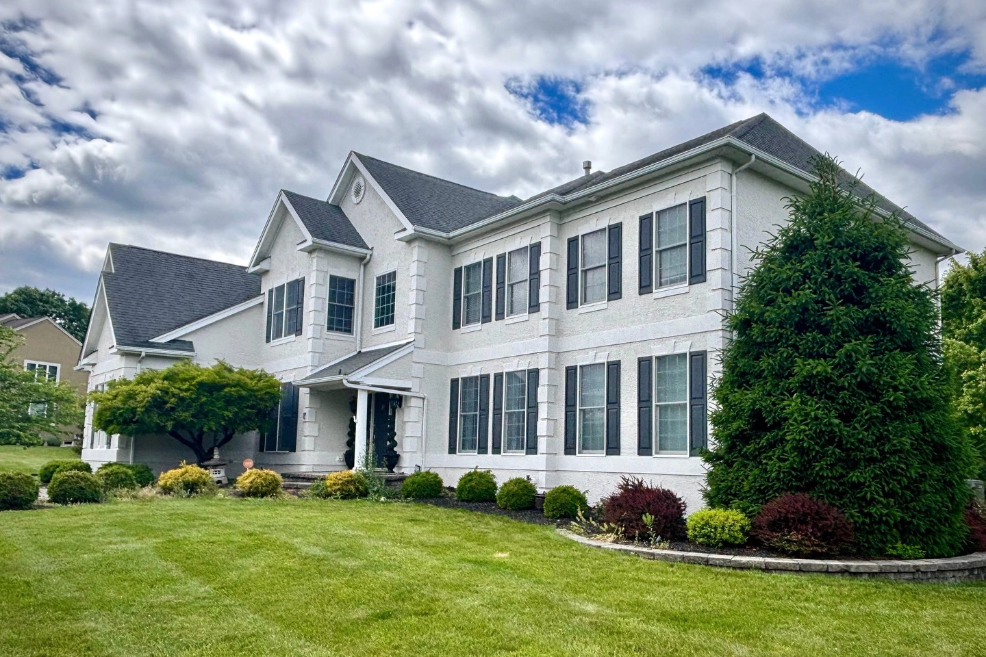 Fully restored two-story home in Flemington NJ with pristine white stucco facade, featuring multiple large windows, professional landscaping, and properly sealed exterior after complete stucco restoration project