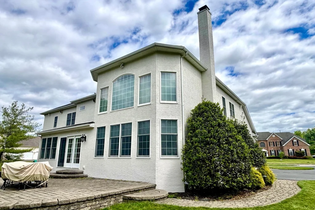 Complete House Stucco Restoration in Flemington, NJ: A Case Study 3 Completed stucco restoration on rear elevation of Flemington home with restored patio area, showing pristine white stucco finish, sealed windows, and professional elastomeric coating protecting the entire exterior