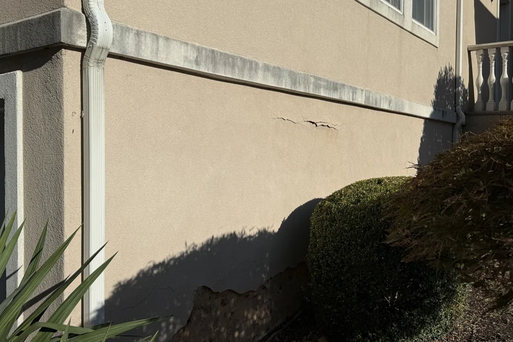 Horizontal crack and crumbling base coat on a stucco exterior wall in New Jersey — a visible warning sign of water infiltration and potential wood rot behind the surface