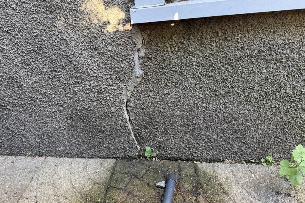 Wide vertical structural crack in exterior stucco with moisture staining and delamination on a New Jersey home — a major red flag identified during pre-purchase stucco inspection