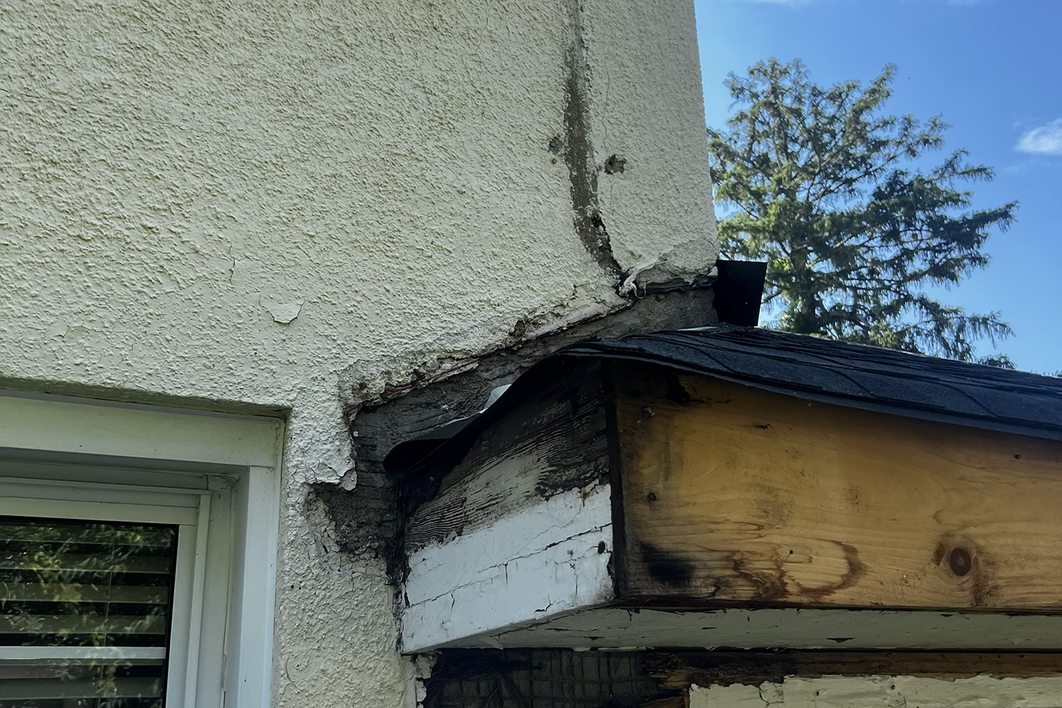 Exposed rotted wood framing and black mold behind failed stucco at roof-wall junction on a New Jersey house — result of missing kickout flashing and moisture intrusion